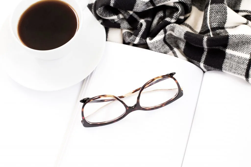 white coffee mug filled with black coffee on white desk with black glass frames and black and white plaid scarf