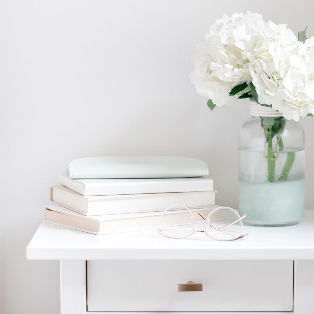 white fresh flowers in vase on bedside table against white wall