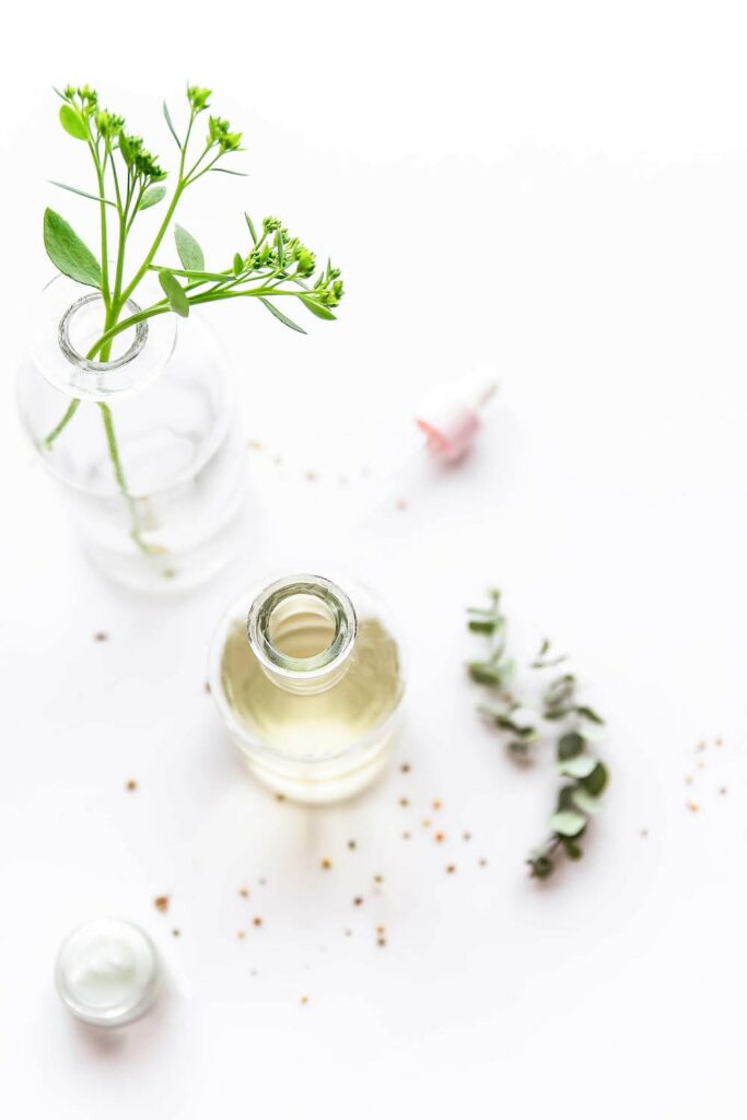 glass bottle of oil on white background with greenery in vase