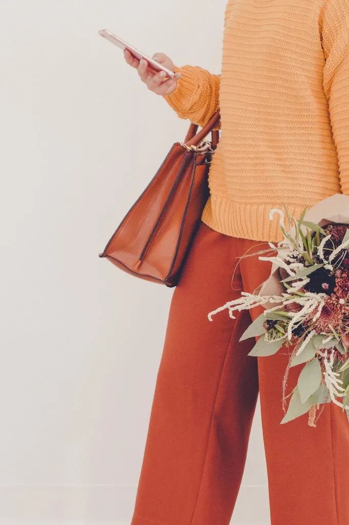 woman wearing orange pants and orange sweater holding flowers