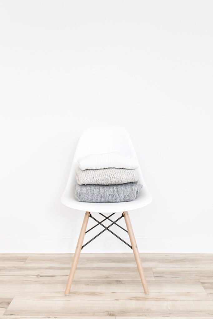 grey and white sweaters stacked on a white chair