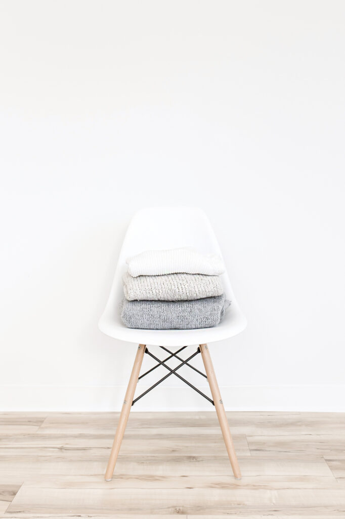 grey and white sweaters stacked on a white chair
