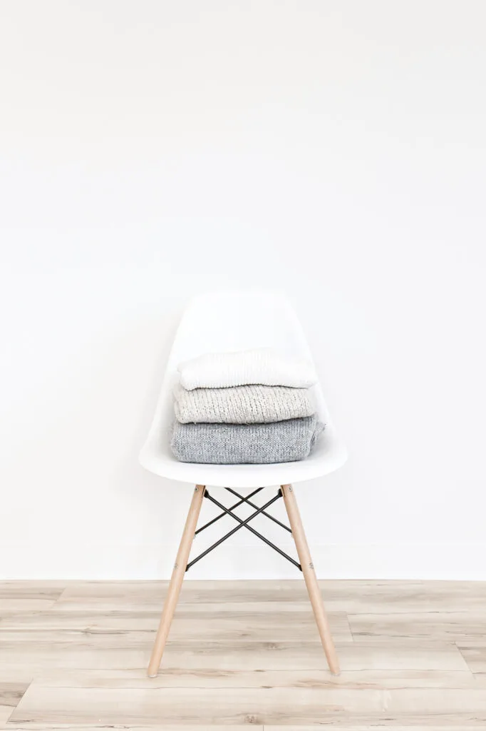 grey and white sweaters stacked on a white chair