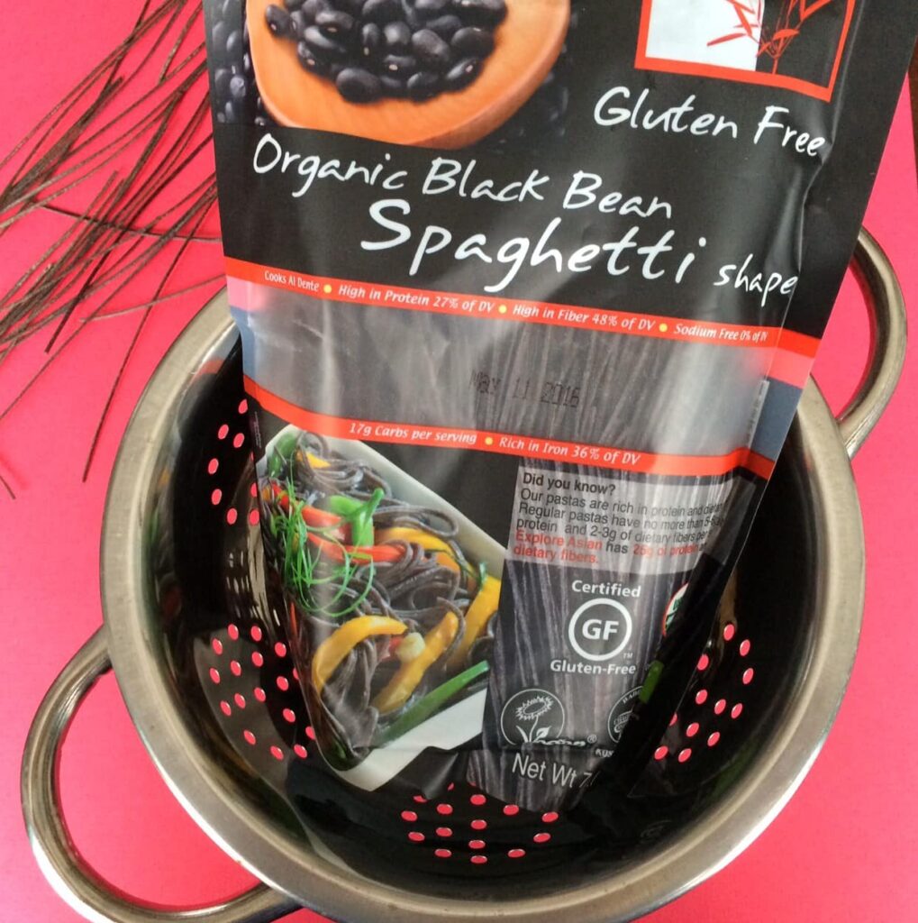stainless steel colander filled with black bean pasta against a red background