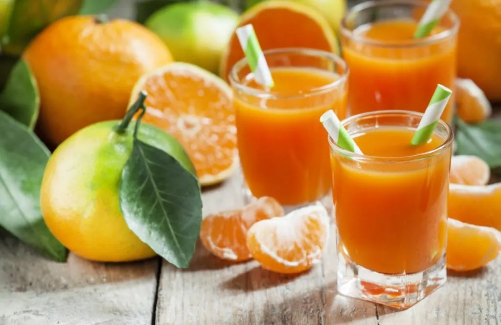 Fresh juice of ripe mandarins in a small glass with striped straw