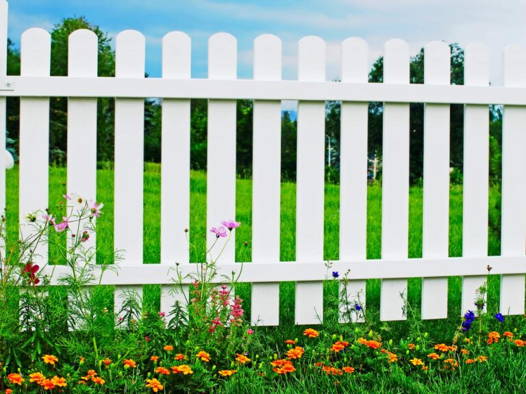White wooden fence on green grass with flowers