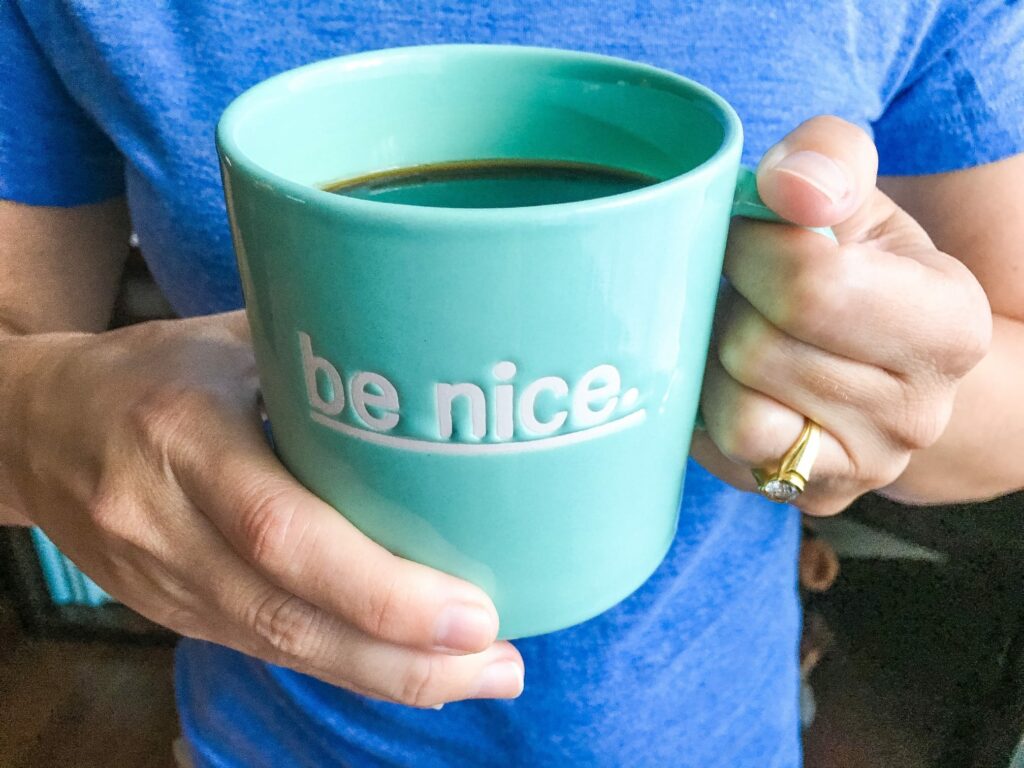 woman holding blue coffee cup with words be nice 