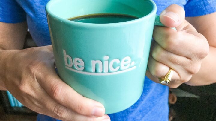woman holding blue coffee cup with words be nice
