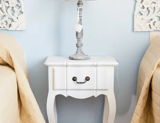 white wooden nightstand with silver lamp on top between two twin beds with linen comforters