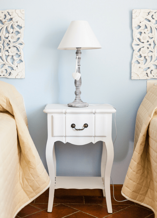 white wooden nightstand with silver lamp on top between two twin beds with linen comforters