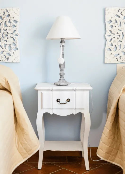 white wooden nightstand with silver lamp on top between two twin beds with linen comforters