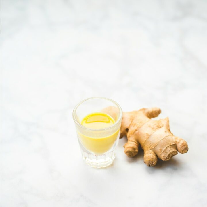 ginger root on marble table next to small glass of orange juice