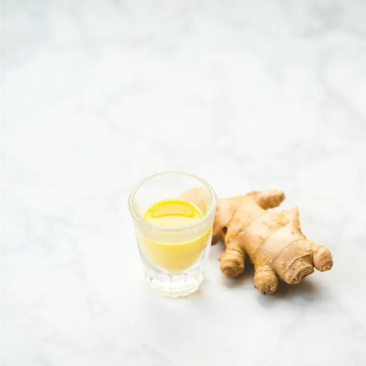 ginger root on marble table next to small glass of orange juice