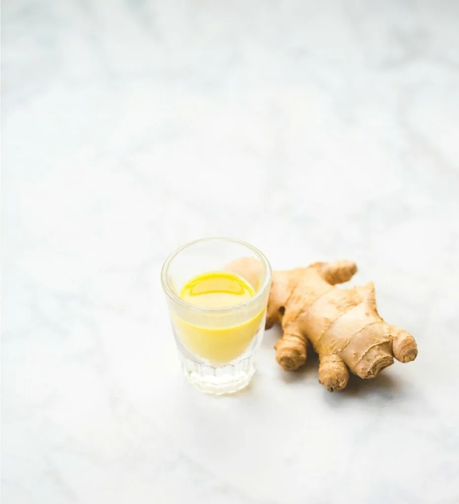ginger root on marble table next to small glass of orange juice