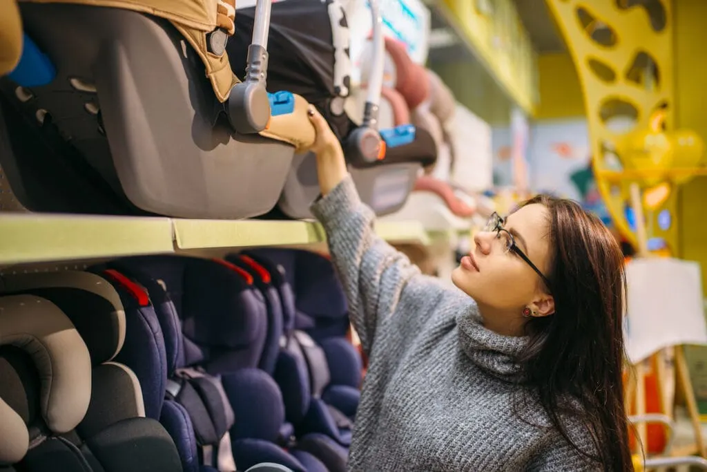 Pregnant woman choosing child car seat in store. 