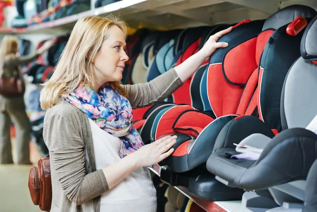 woman choosing child car seat for newborn baby in shop