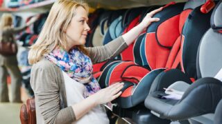 woman choosing child car seat for newborn baby in shop