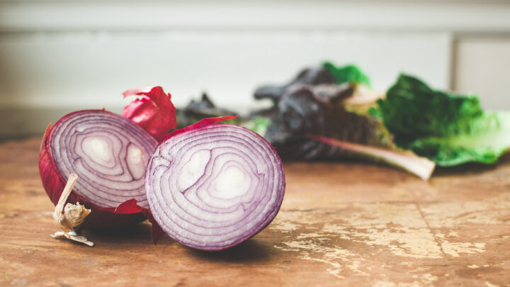 red onion cut in half on wooden cutting board