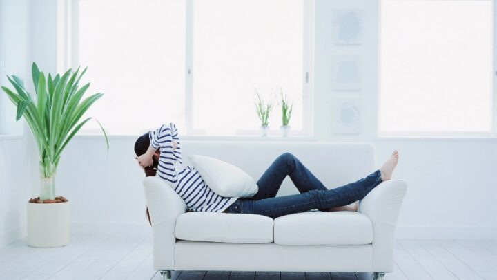 woman relaxing on white couch in white room with lots of windows and minimalistic decor