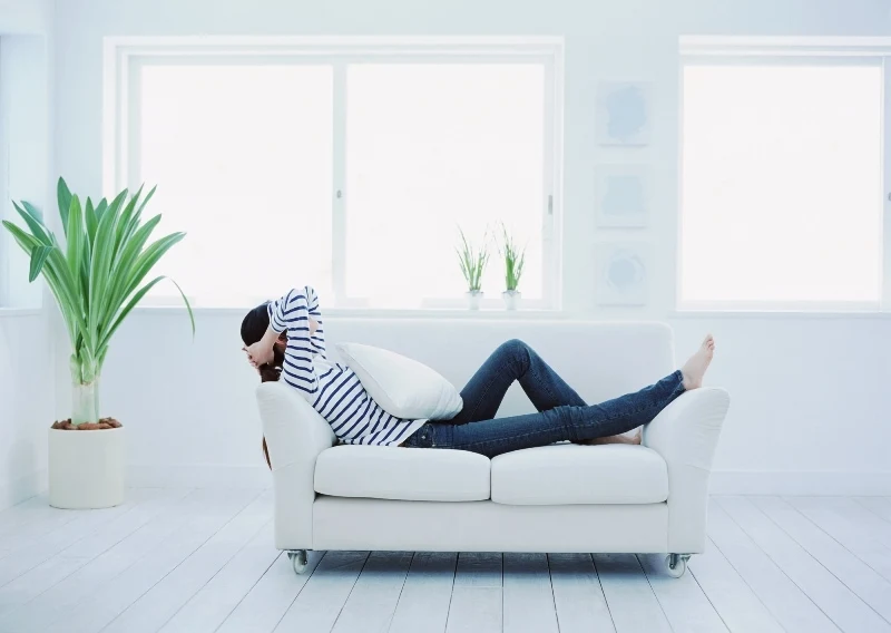 woman relaxing on white couch in white room with lots of windows and minimalistic decor