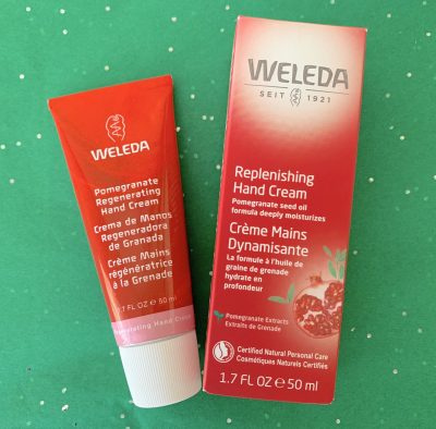 red bottle Pomegranate Replenishing Hand Cream Weleda against green background