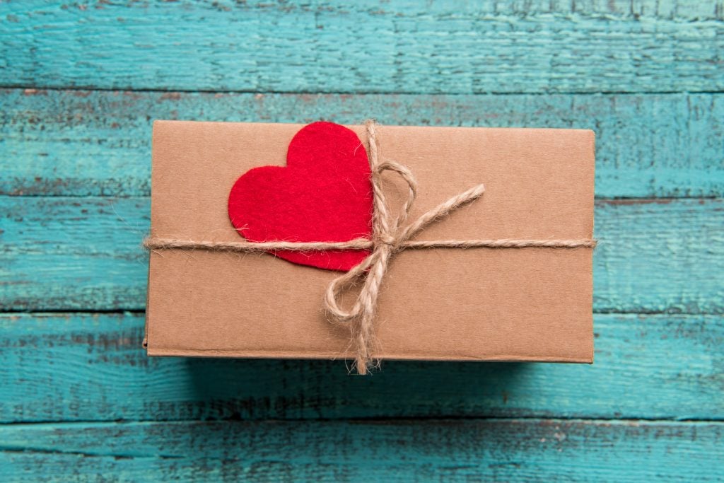 gift wrapped in brown paper with twine bow and red felt heart against blue wooden slat backdrop