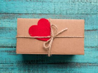gift wrapped in brown paper with twine bow and red felt heart against blue wooden slat backdrop