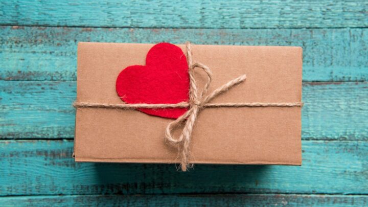 gift wrapped in brown paper with twine bow and red felt heart against blue wooden slat backdrop