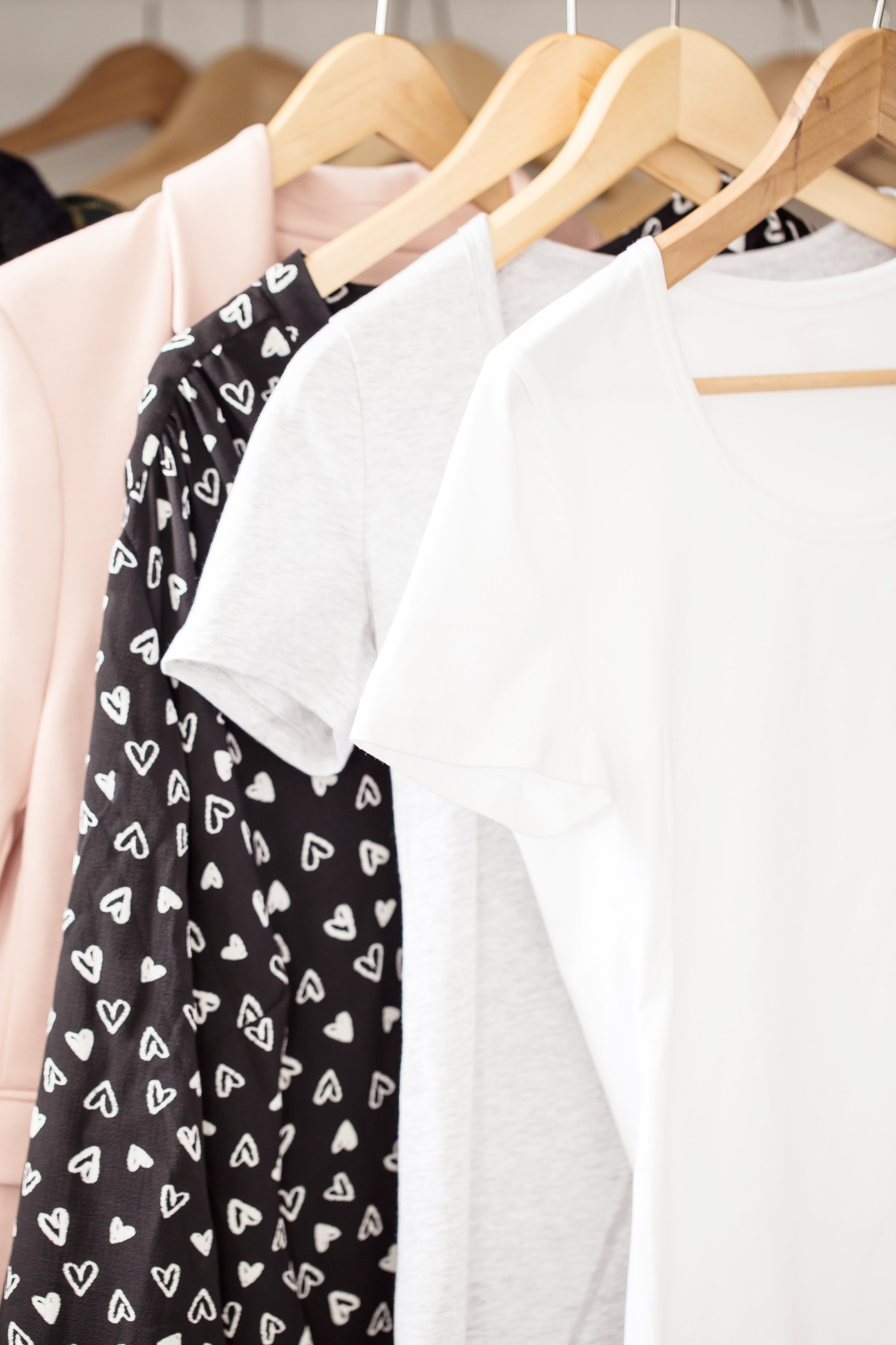 white black and pink women's clothing hangin on wooden hangers in closet