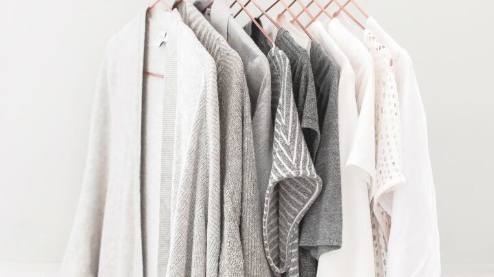 womens clothes in shades of white and grey hanging on copper hangers on curtain rod