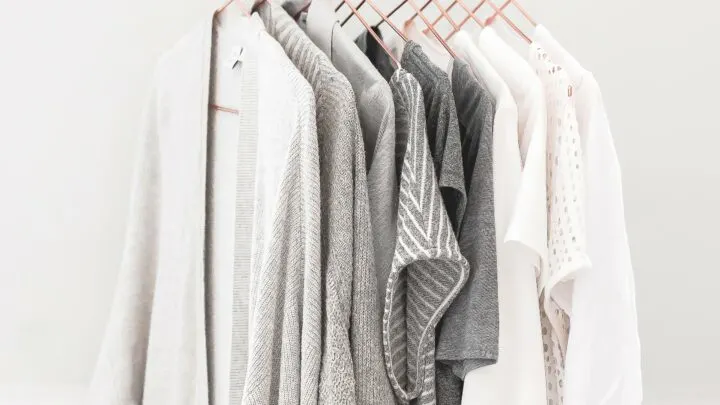 womens clothes in shades of white and grey hanging on copper hangers on curtain rod