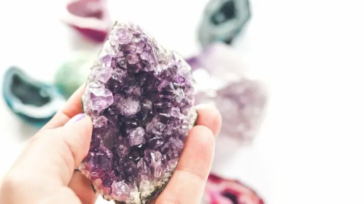 woman holding a purple crystal against colorful geodes