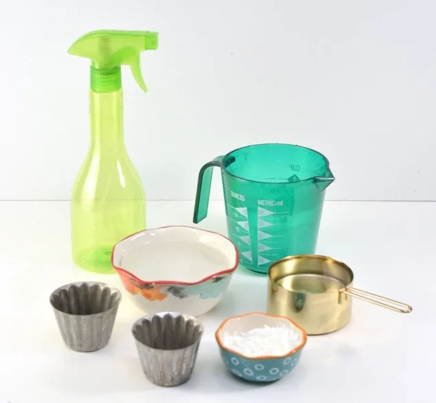 green spray bottle blue measuring cup measuring dishes on white countertop