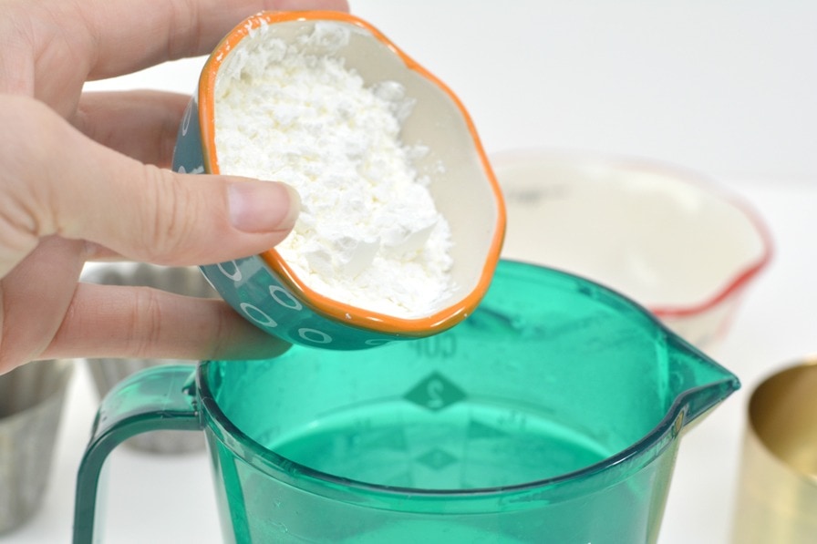 small bowl of cornstarch being poured into blue measuring cup