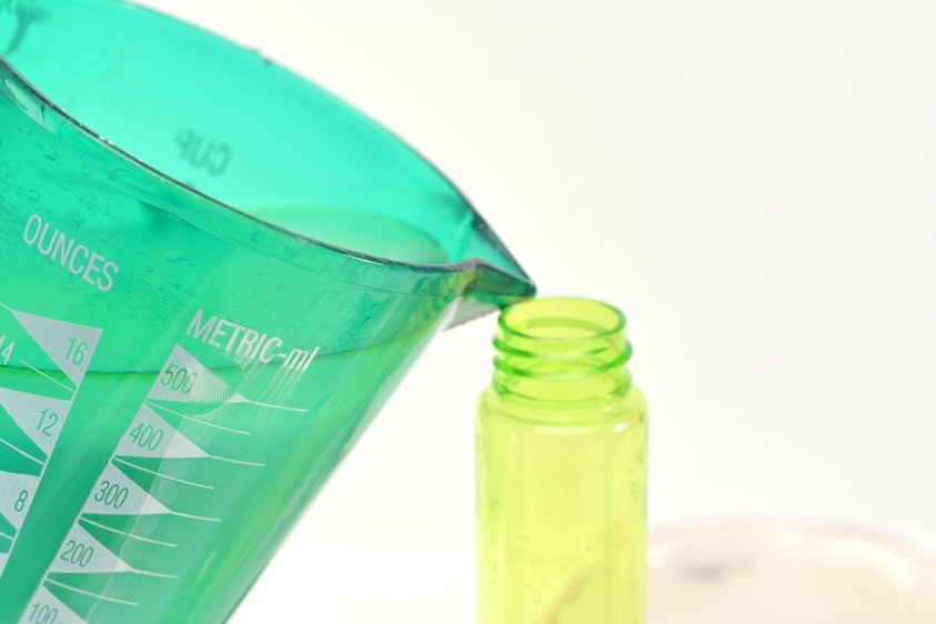 blue measuring cup pouring liquid into a green spray bottle