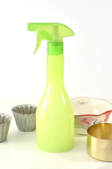green spray bottle with measuring cups on table around it