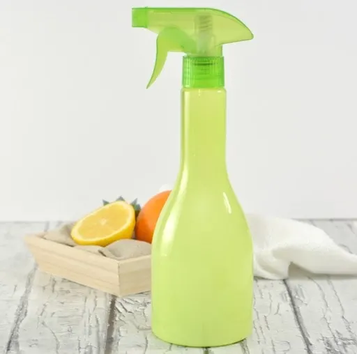 green spray bottle on wood table with box of oranges and white cloth behind it