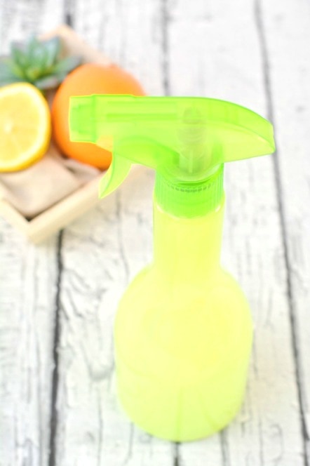 green spray bottle with oranges beside on wooden table