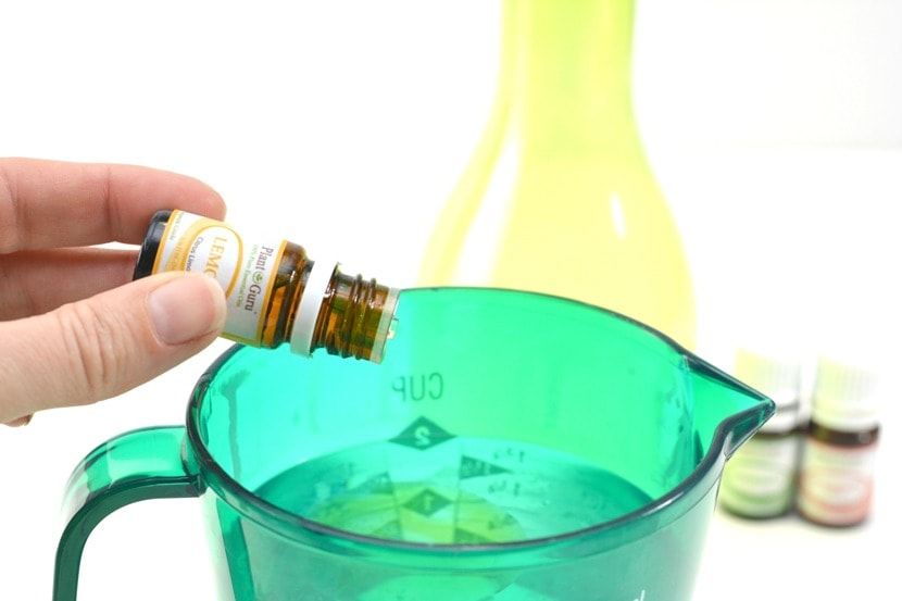 dropping lemon essential oil into a measuring cup of liquid cleaner