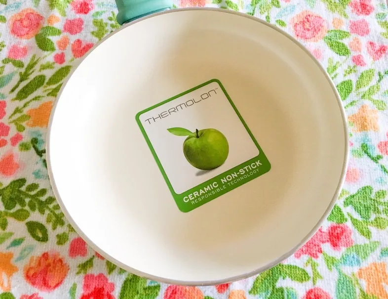 thermolon sticker with green apple on nonstick ceramic cookware pan against colorful flower towel