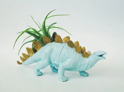 plastic dinosaur painted baby blue with gold spikes and air plant growing out of back
