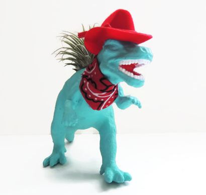 blue plastic dinosaur dressed up like a cowboy with a red hat and a red bandana and air plant growing in back