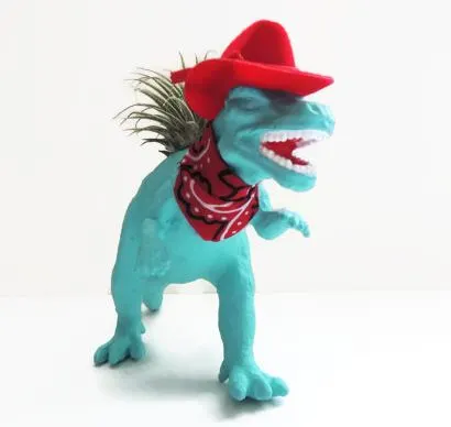 blue plastic dinosaur dressed up like a cowboy with a red hat and a red bandana and air plant growing in back