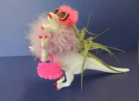 white plastic dinosaur wearing a purple feather boa pink sunglasses purse and red painted nails