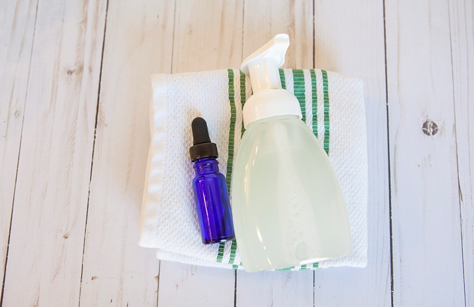 foaming hand soap dispenser on a white hand towel with blue essential oil glass bottle 