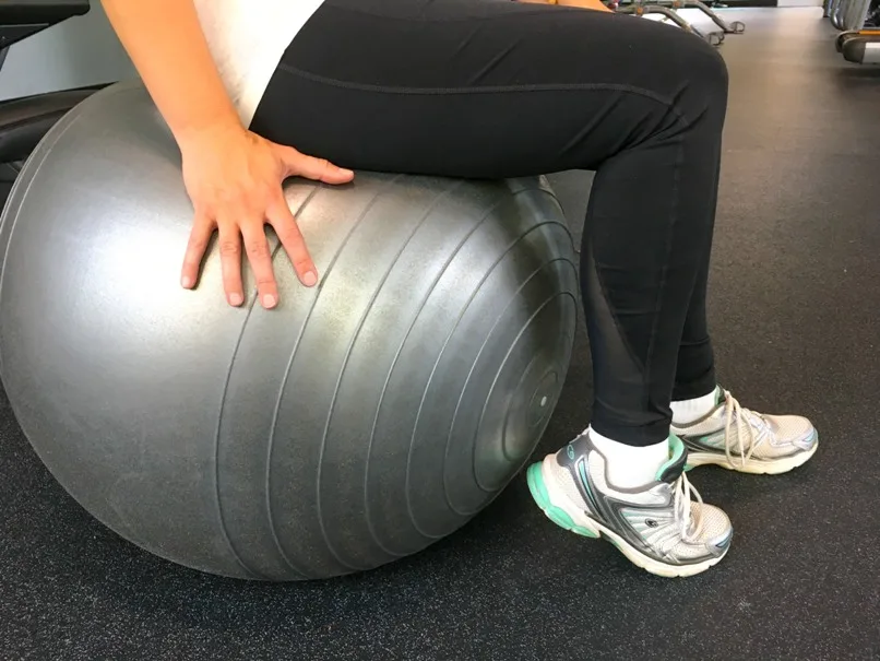 sitting on grey workout ball wearing black leggings