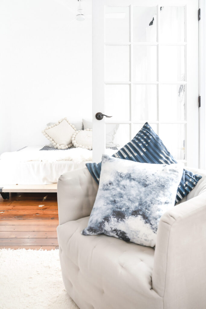 tan upholstered chair with blue throw pillows on white carpet