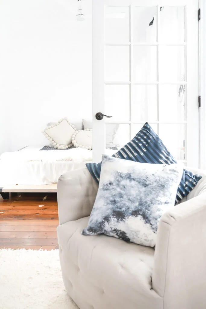 tan upholstered chair with blue throw pillows on white carpet