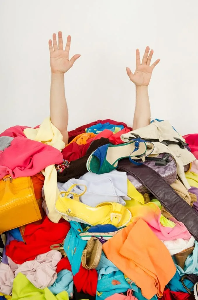 woman under a pile of clothes and shoes with hands up in the air