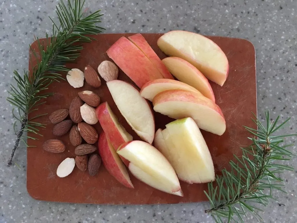 cutting board with apples almonds and pine branches